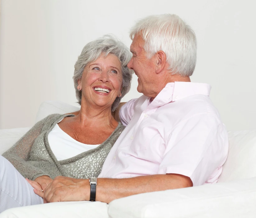 Smiling senior Caucasian couple sitting comfortably on a sofa in a bright room full of books.
