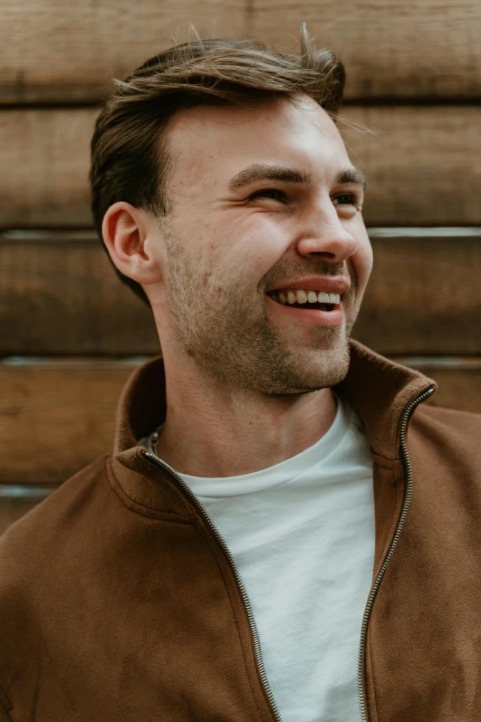 Candid portrait of a smiling man in casual attire against a wooden backdrop in Berlin.